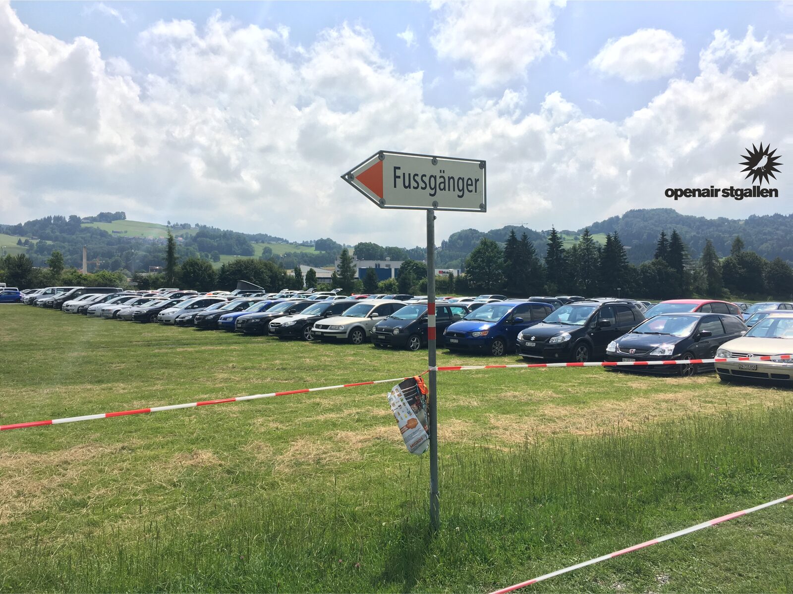 Pedestrian wayfinding signage at a grass event parking area.